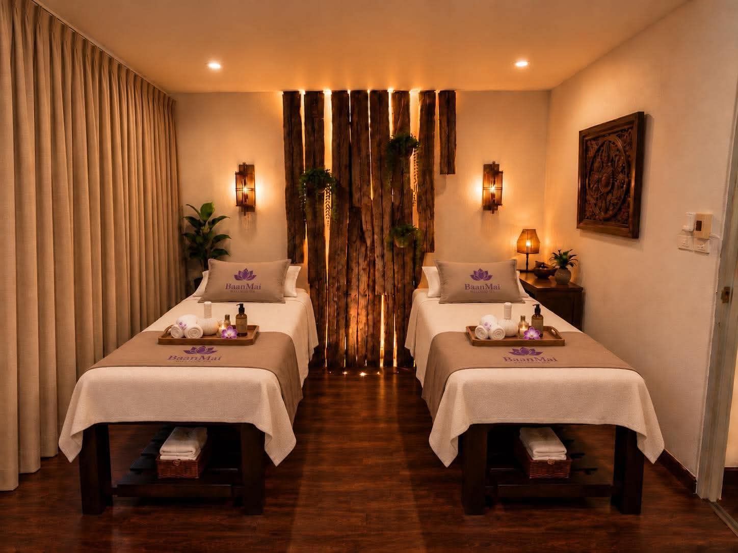 Two massage beds in front of a screen of lit timber planks, with wall lamps either side.